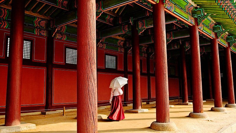 A woman, dressed in a tradition Korean hanbok, walking the grounds of Gyeongbokgung Palace in Seoul, Korea