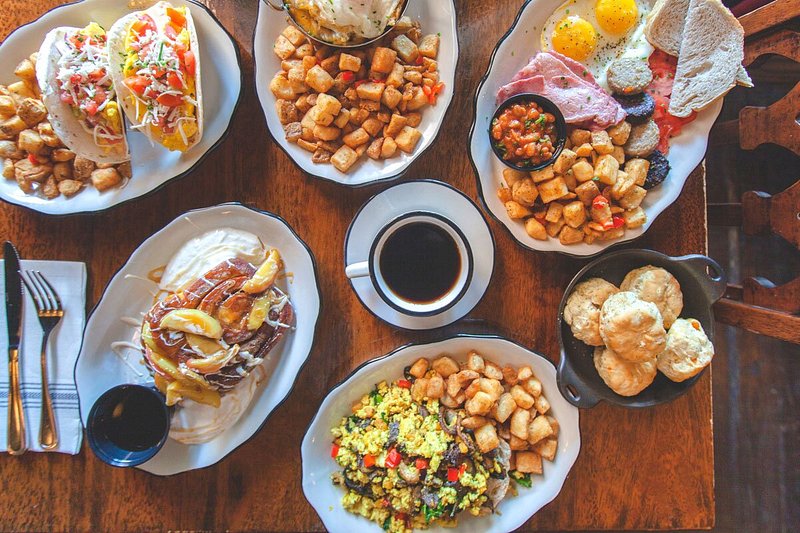 Aerial view of table topped with breakfast dishes such as tacos, potatoes, biscuits, cinnamon roll, and coffee