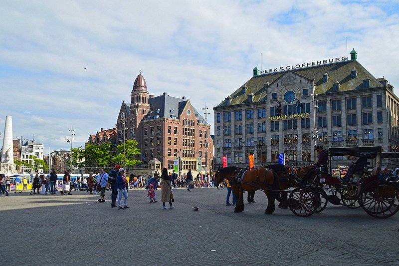 City square with lots of people and horse-drawn carriages, and surrounded by historic buildings