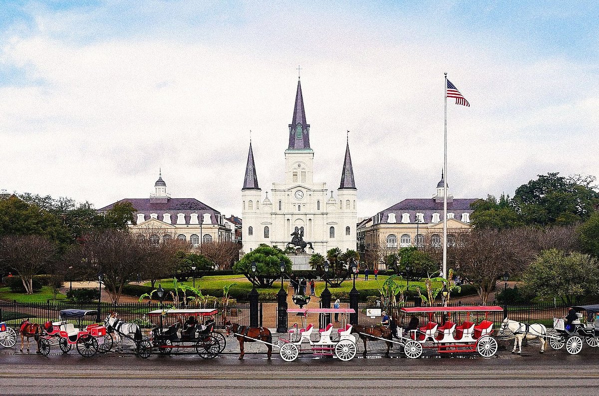 Horse-drawn carriages lined against entrance to Jackson Square. with St. Louis Cathedral behind it
