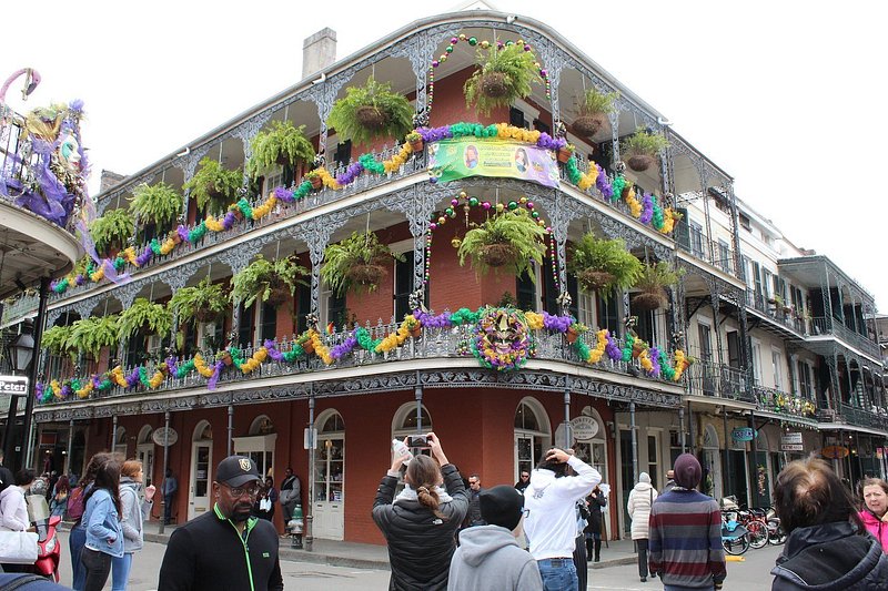 People looking up at building featuring wrought-iron balconies with Mardi Gras decor