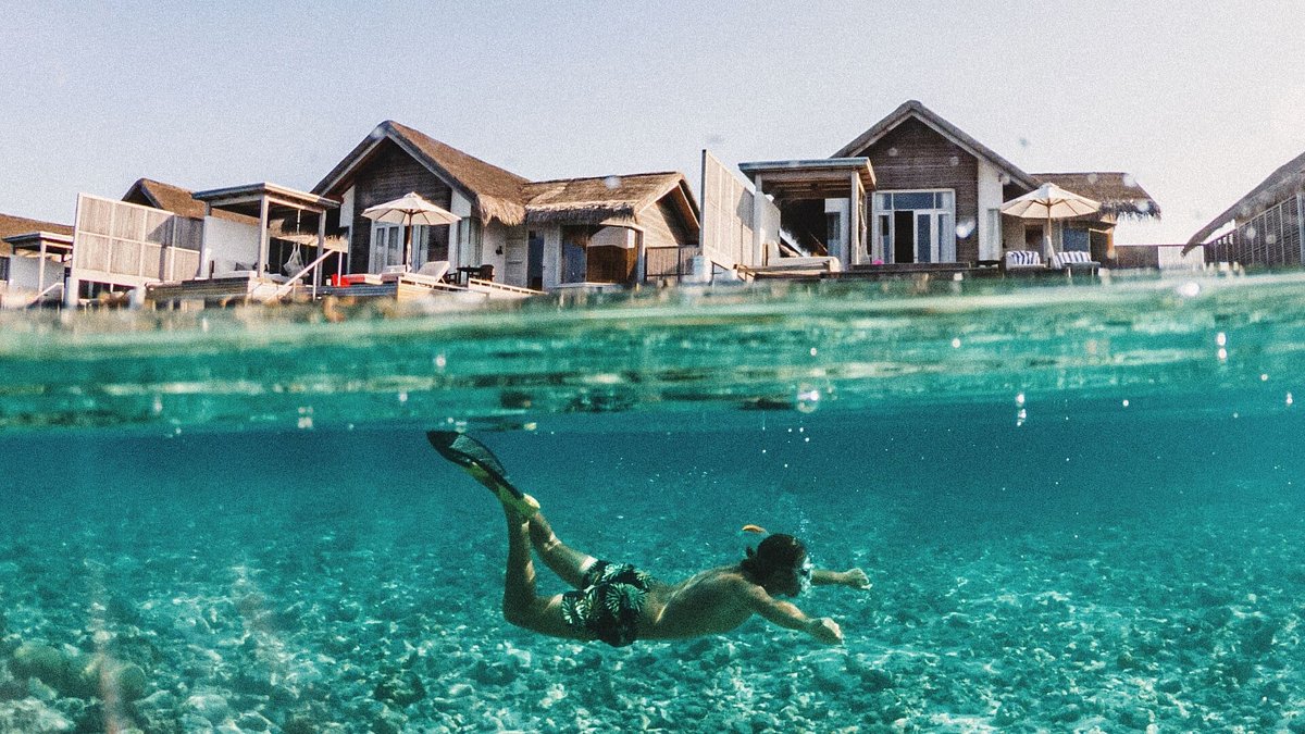 Man som snorklar i havet på Maldiverna med villor över vattnet i bakgrunden.