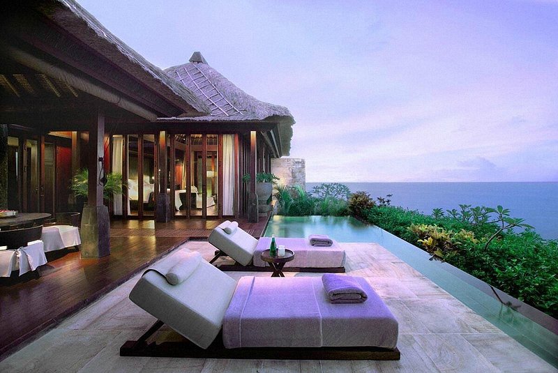 Ligstoelen en overloopzwembad buiten met uitzicht op zee in een resort in Bali, Indonesië.