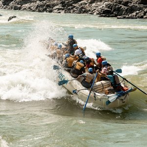 A paddle raft going through a rapid with half of the boat being soaked by the splash. 