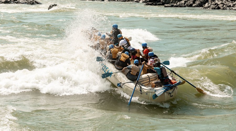 A paddle raft going through a rapid with half of the boat being soaked by the splash. 