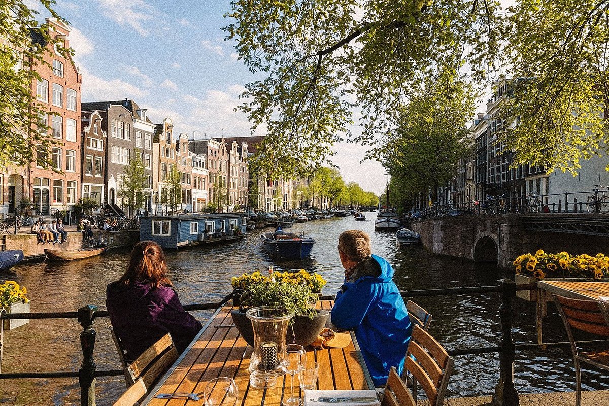 Two people sitting at wooden table looking out over the adjacent canal 