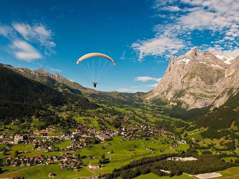 A paraglider flying high above mountains, lakes, and villages in Interlaken, Switzerland
