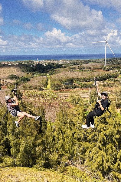 Two travelers racing each other on side-by-side ziplines above Keana Farms
