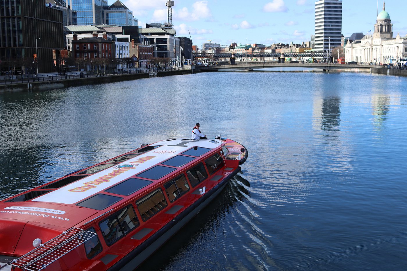 Red tour boat on a river with city buildings in the background.
