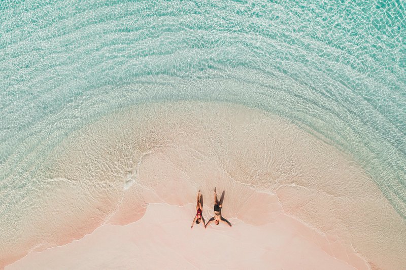 Fotografia tirada de cima de um casal na famosa praia Rosa, no Parque Nacional de Komodo, rodeado por águas azul-turquesa cristalinas