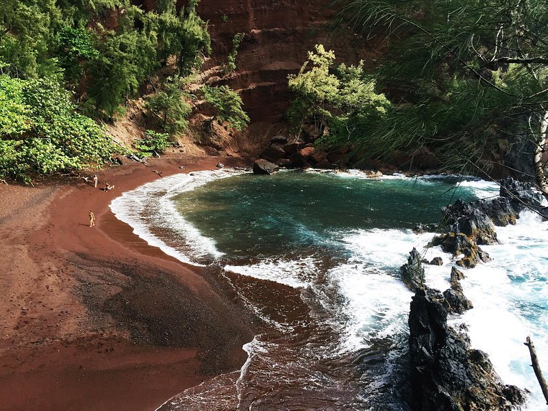 Viajantes a relaxar na praia de areia vermelha de Kaihalulu, em Maui, rodeados de vegetação exuberante e de águas verde-esmeralda