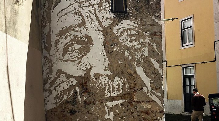 Μια τοιχογραφία με το πρόσωπο ενός γερασμένου άνδρα στο πλάι ενός κτιρίου.