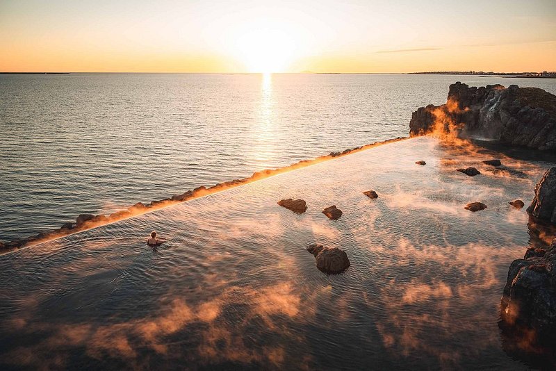 Ένας άνθρωπος σε μια φυσική πισίνα δίπλα στη θάλασσα με θέα στον ωκεανό την ώρα του ηλιοβασιλέματος