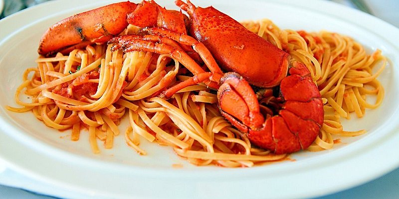 A plate of pasta with a bright red lobster on top