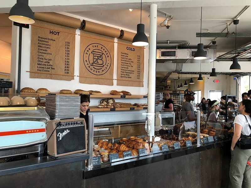 Drink menus on the wall with shelves of bread and a counter full of pastries at Zak the Baker