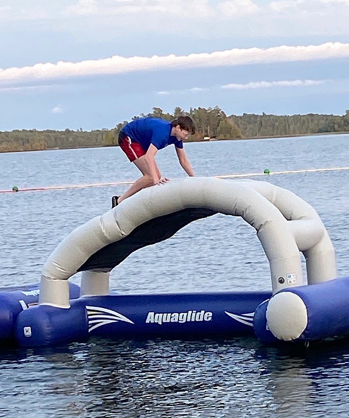 Teen boy fishing from a dock on a lake with brothers swimming