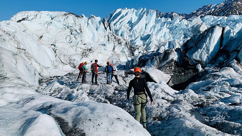 People with safety gear climb on top of a glacier