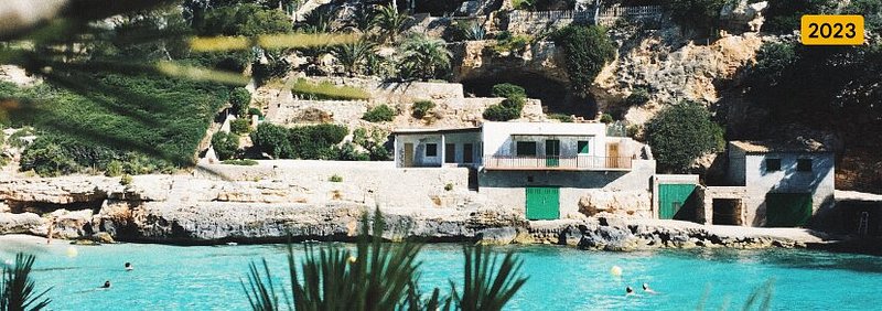Reizigers die zwemmen in de buurt van een rotsachtige waterkant, met daarboven een schilderachtige villa