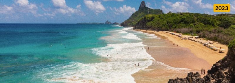 An aerial view of a sandy beach surrounded by sea and mountains