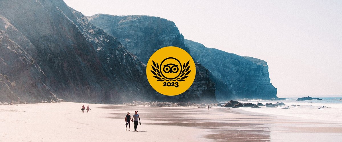 Due persone che camminano lungo la riva della spiaggia di Praia de Vale Figueiras in Portogallo, con il logo Travellers' Choice Best of the Best di Tripadvisor sovrapposto