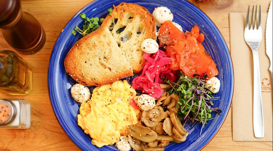 Pan tostado acompañado de salmón ahumado, champiñones, queso crema, huevo revuelto ,cebolla roja encurtida , micromezclum y sésamo negro.