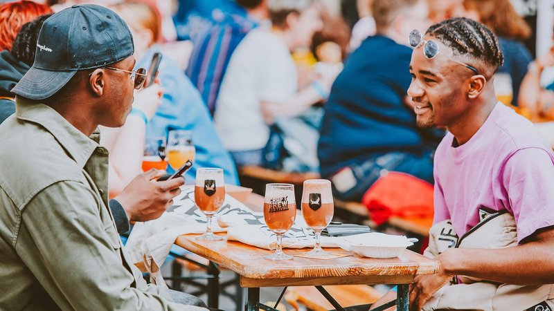 Two men siting across from each other at a table with beer glasses set atop.