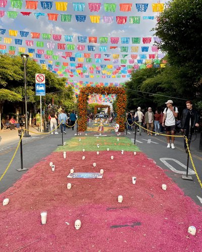 A street decorated for a dia de los Muertos celebration in Tlaquepaque, including floral arches, strings of multi-colored flags and swaths of fabric with skull displays
