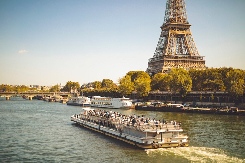 Travellers cruising down the Seine River on a ferry, with the Eiffel Tower and golden autumn foliage in the background
