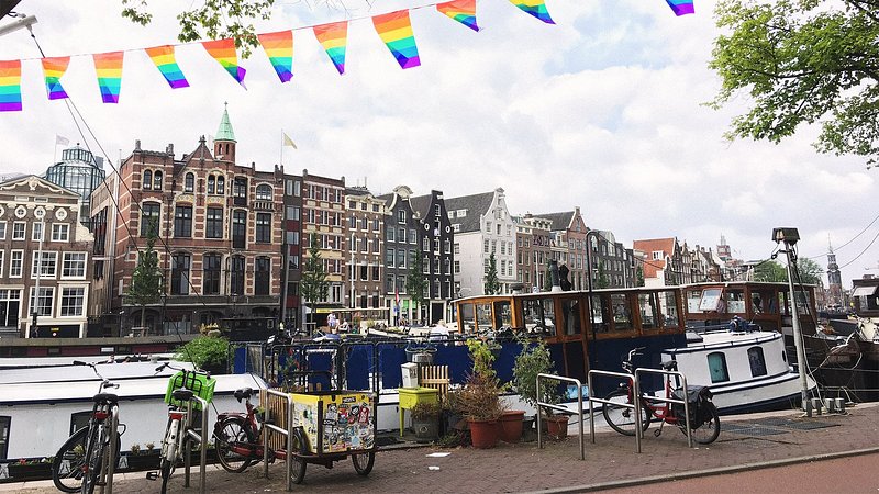 A street in Amsterdam overlooking the canal, dotted with boats, as well as the canal buildings in the background