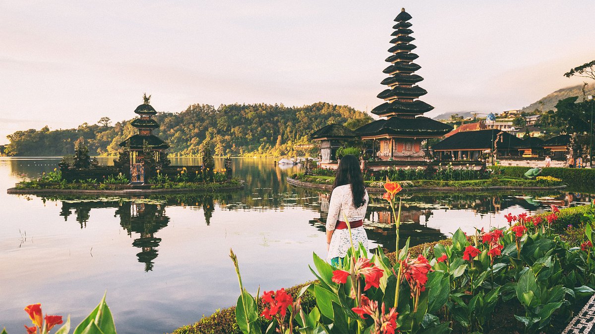 A woman stands looking out over the water and foliage surrounding a traditional Balinese temple