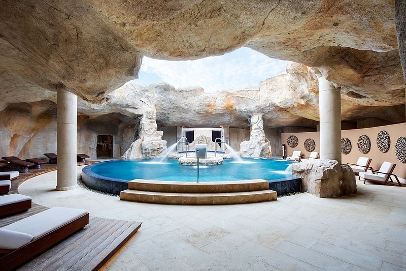 Open air cavern with a hydrotherapy pool and a circle of reclining chairs and yoga beds