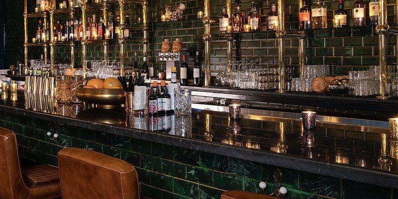 A bar with dark green tiles and brass accents.