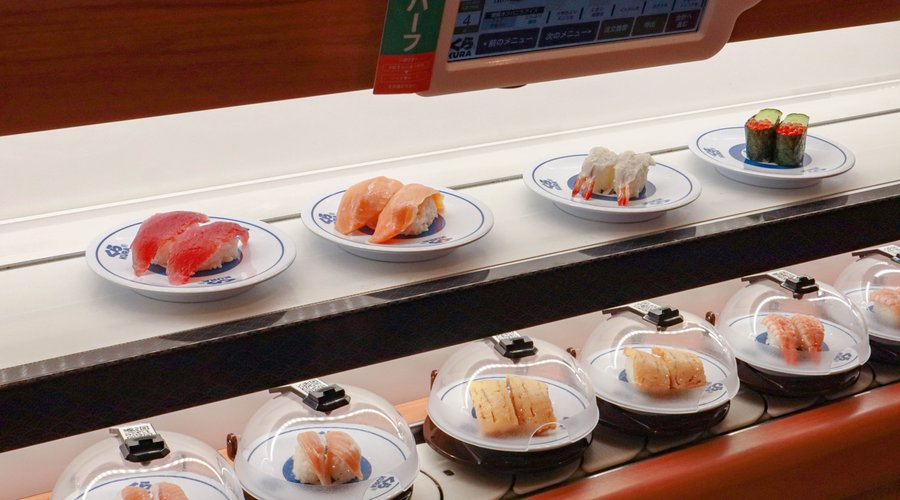 くら寿司では、タッチパネルでご注文いただいた商品を素早くお客様にお届けするオーダーレーンを導入。単にベルトの上に商品を乗せ流すことで、受け皿を厨房へ戻すタイムロスを省き、出来たての味をそのまま厨房からお届けできるシステムです。これにより、注文を受けてから作る揚げたての天ぷら、ラーメンやかき氷などもご提供できるようになりました。また、当社独自の「抗菌寿司カバー」があるからこそ可能な回転レーンでの安全・安心な商品のご提供も行っており、パレードのようにお寿司が続々と流れてくる、回転寿司ならではのワクワク感も大切にしています。全店でオーダーレーンと回転レーンの両方を活用する「二刀流レーン」で商品をご提供しているのは今や業界で唯一となっており、お客様の様々なニーズにお応えできるようにしております。
