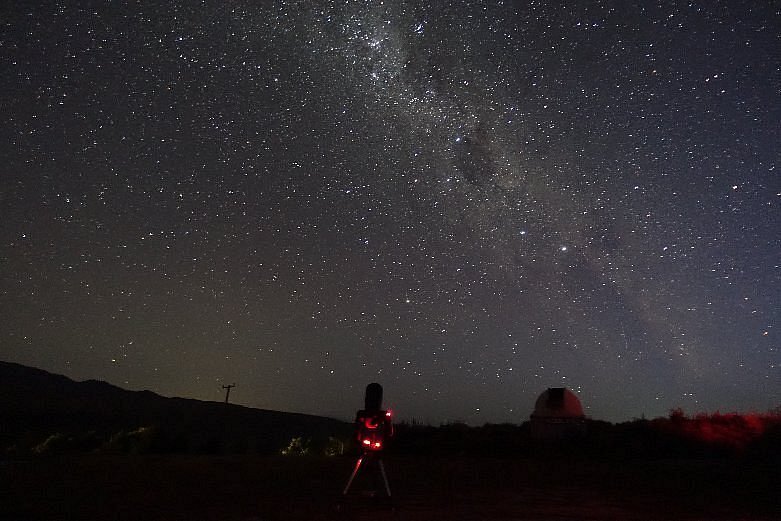 En resenär som tittar upp mot en himmel full av stjärnor vid Lake Tekapo, Sydön, Nya Zeeland.