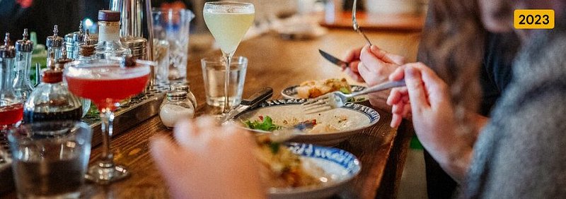 “Hands of two people drinking dining at a warmly lit restaurant bar”