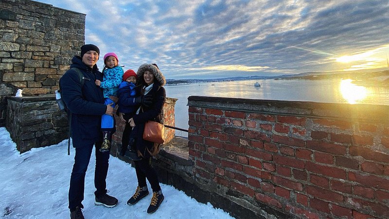 A family of four stands in a snowy bank overlooking a sunset