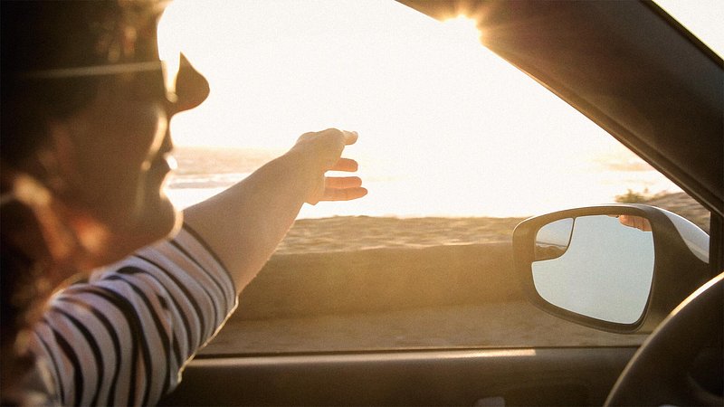 A woman holds her hand out the rolled-down window of her car while driving