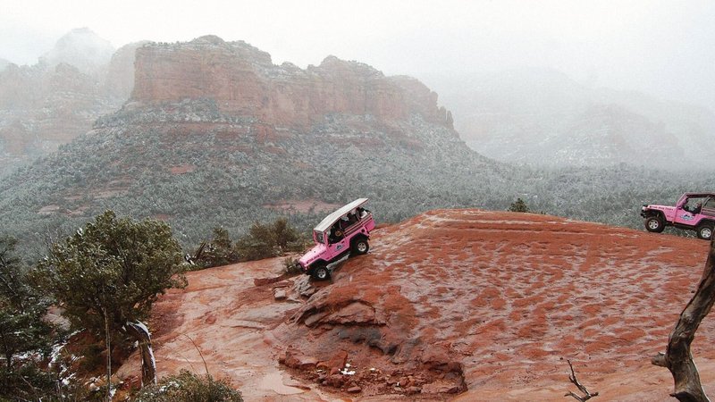 A pink jeep descends down a mountainside in the snow