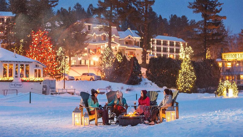 Friends sitting around bonfire at Mirror Lake Inn and Resort, in Lake Placid, in the winter