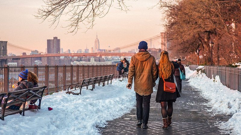 Couple walking in winter along the promenade in Brooklyn Bridge Park with view of Manhattan