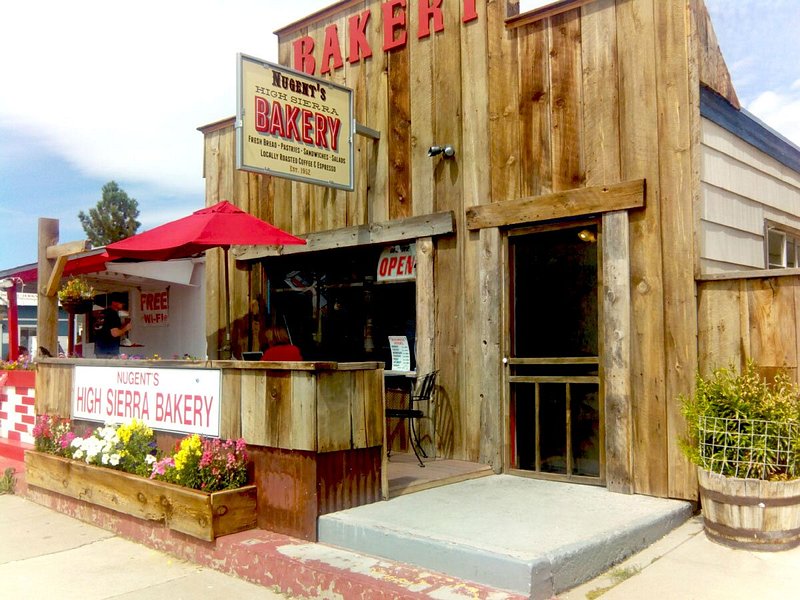 Exterior of wooden bakery with red umbrella over patio seating
