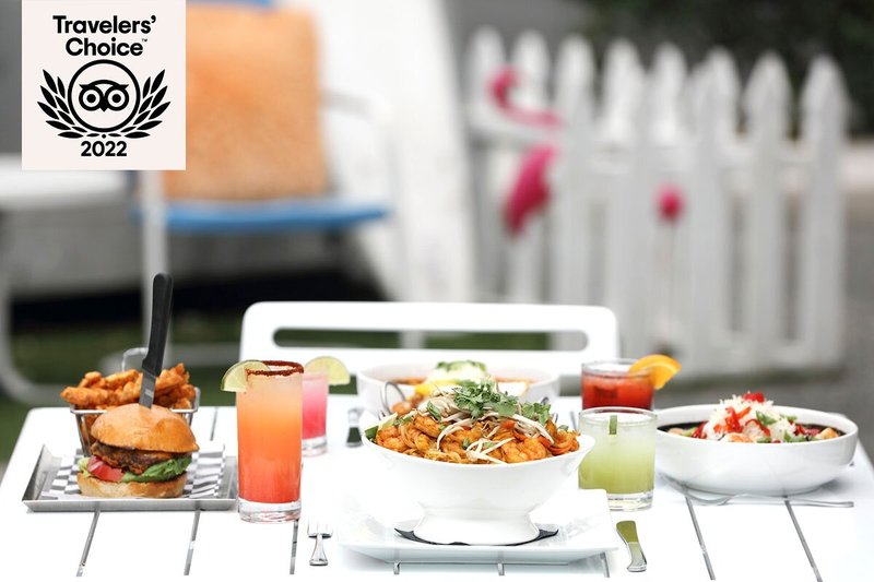 White outdoor table topped with cocktails and dishes like a burger