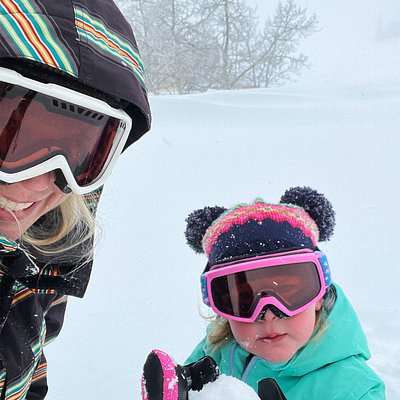 A toddler holds a handmade snowball on ski slope