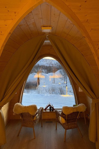 Interior of a cozy Gamme cabin at Snowhotel Kirkenses, with two chairs facing an arched picture window