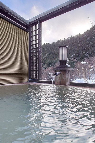 An open-air onsen in a ryokan with sweeping views of a nearby forest