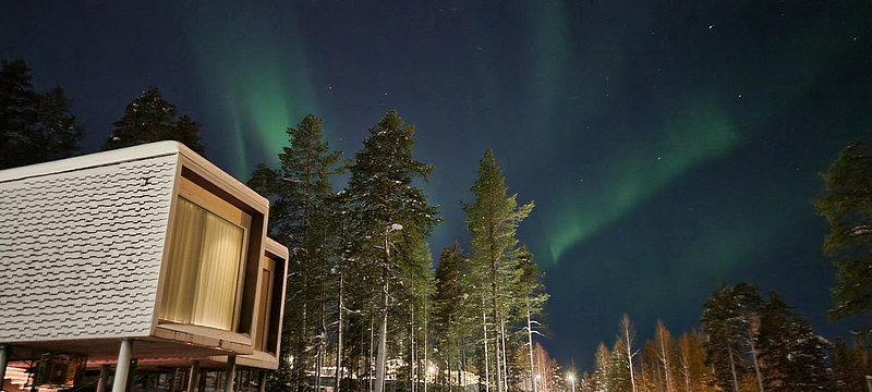 Exterior view of the stylish suites at the Arctic TreeHouse Hotel in Rovaniemi, with the Northern Lights in the background