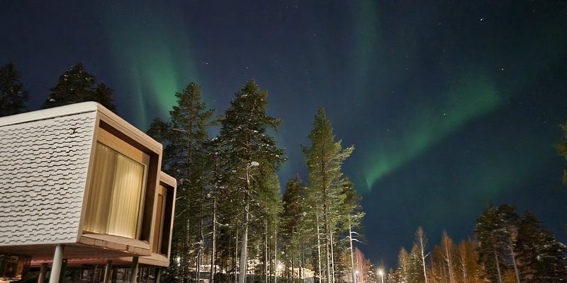 Exterior view of the stylish suites at the Arctic TreeHouse Hotel in Rovaniemi, with the Northern Lights in the background.