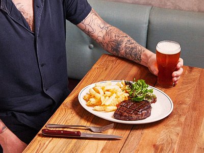 A man drinking a beer and eating a steak with fries at Forrester's