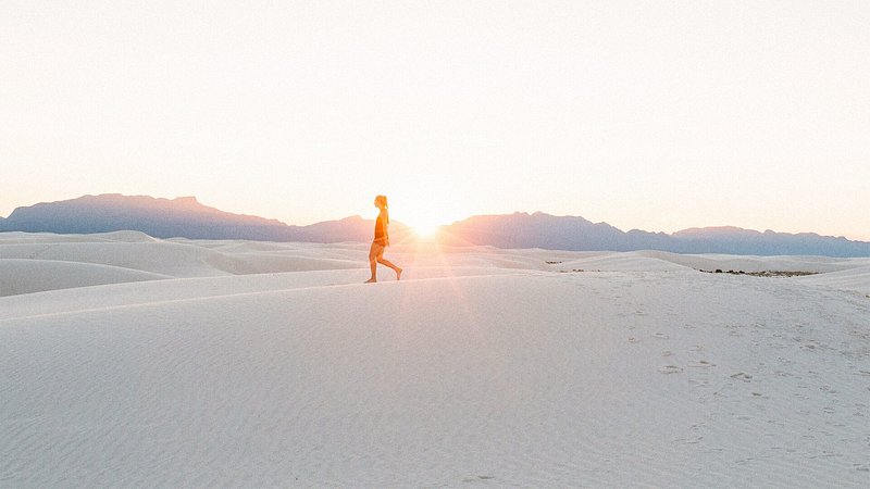 Woman walking on sand dunes at White Sands National Park at sunset