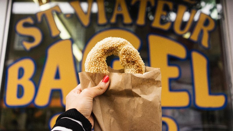 Woman holding up Montreal bagel in front of St. Viateur Bagel Shop